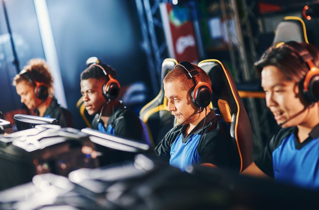 Team of four professional cybersport gamers wearing headphones participating in eSport tournament, playing online video games while sitting in gaming club or internet cafe, selective focus