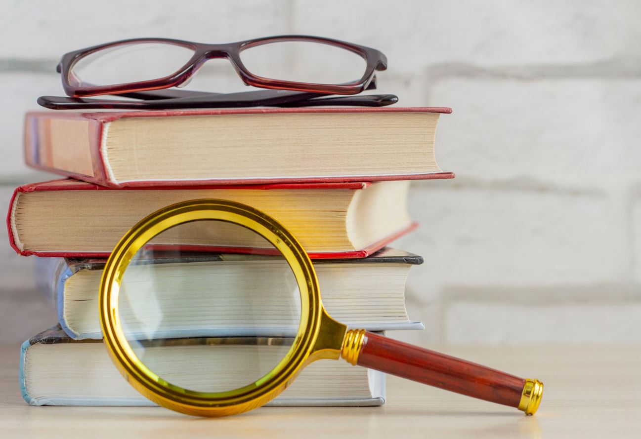 A stack of books, glasses, and a magnifying glass on the table.The concept of information search. stock photo