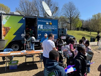 Children gather around a large, colorful van with a satellite dish on top, engaging in an educational outreach program.