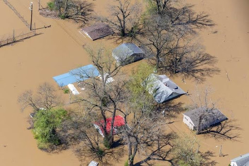 Aerial view of several houses partially submerged in muddy floodwaters.
