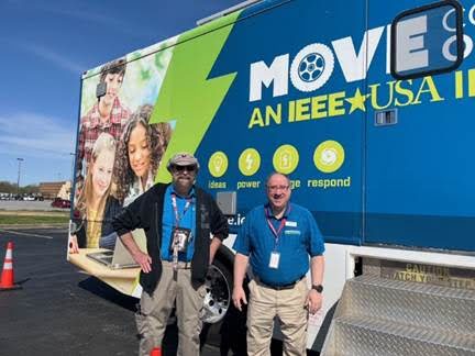 Two staff members pose in front of the MOVE truck, which features colorful graphics of students engaging in STEM activities.